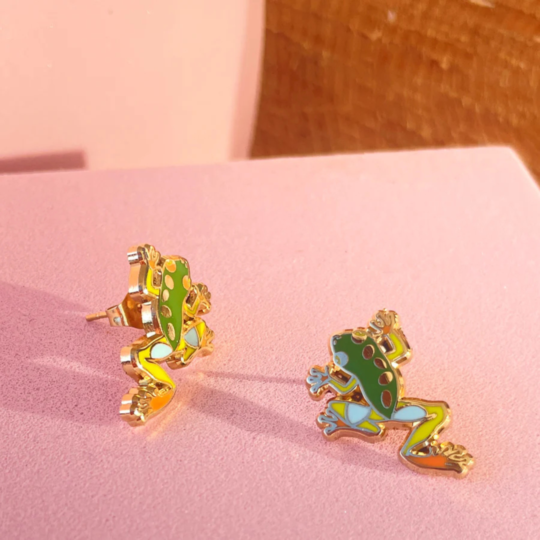 Frog-shaped earrings on a pink surface.
