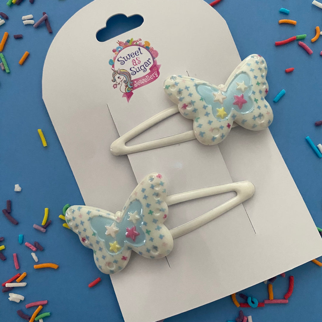 A blue butterfly hair clip with white star patterns attached to a white metal snap clip.