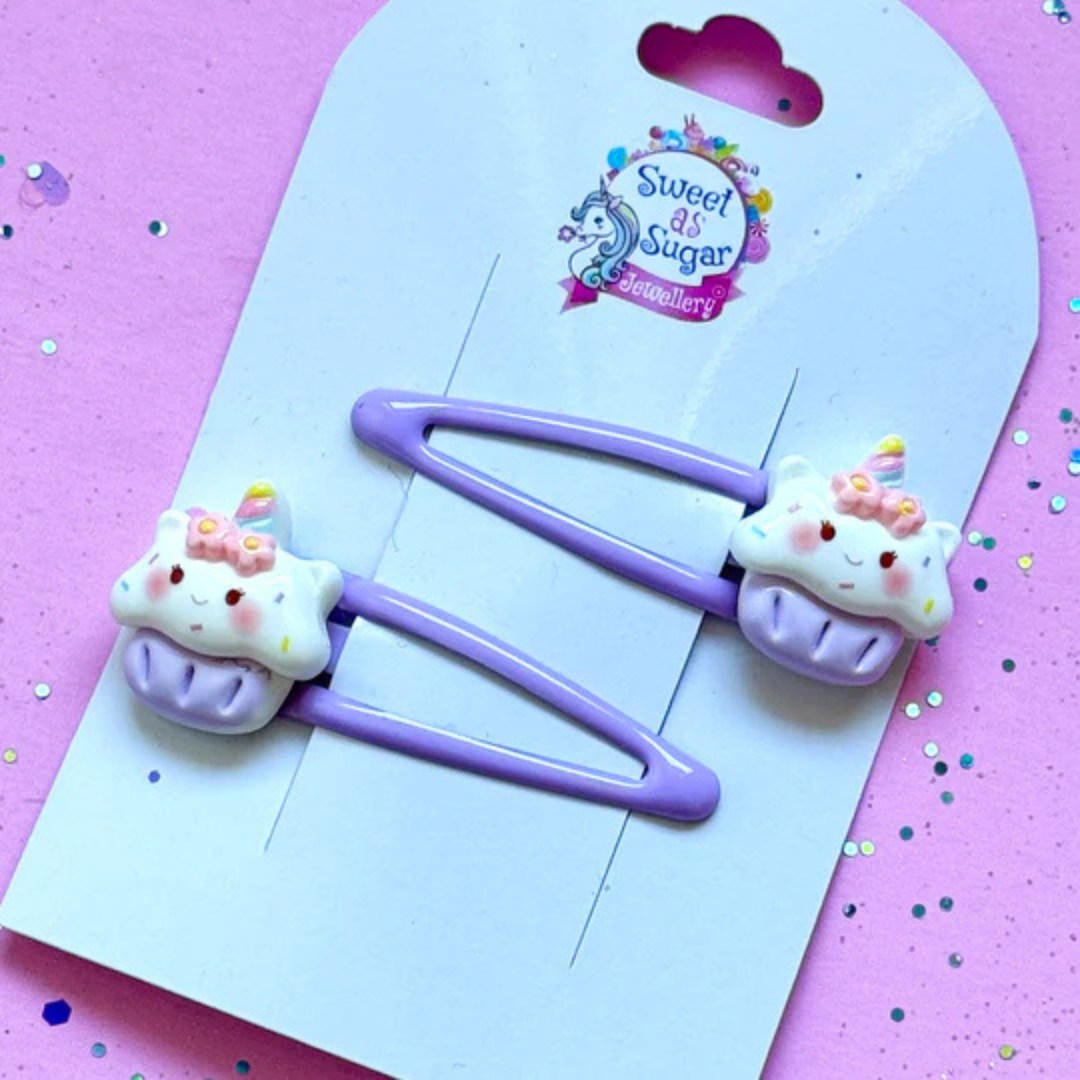 A cupcake-themed hair clip featuring a colourful cupcake charm with frosting and sprinkles, attached to a lilac metal snap clip.