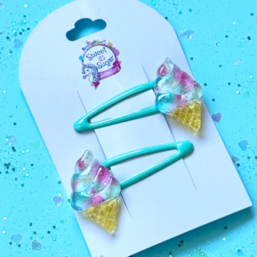 A hair clip featuring a colourful ice cream scoop on a golden cone charm, attached to a vibrant aqua-blue metal snap clip.