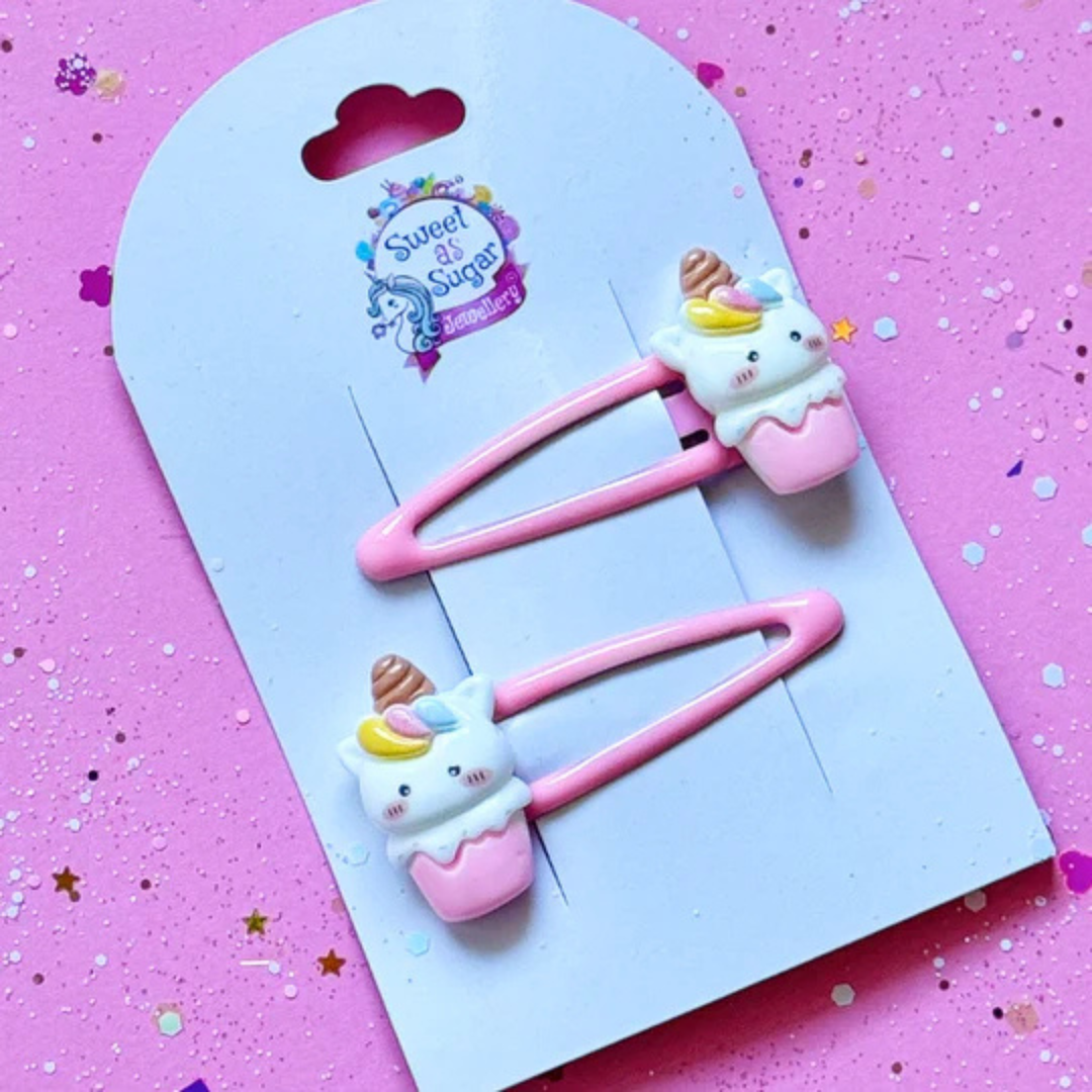 A unicorn ice cream hair clip featuring a white unicorn with a golden horn tucked into a pink cone cup, attached to a matching pink metal snap clip.