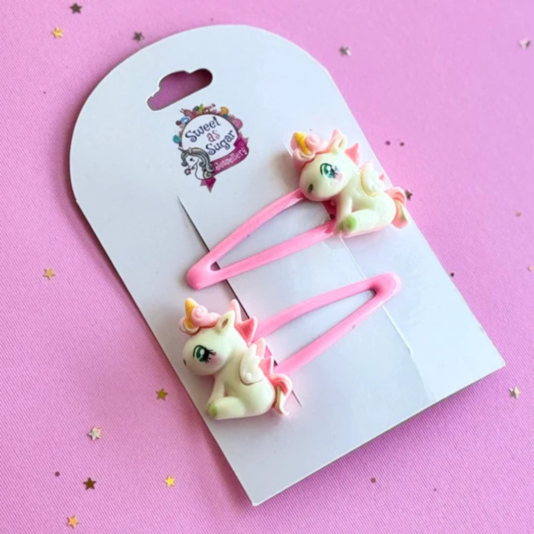 A unicorn pony hair clip featuring a white sitting pony with a colourful mane, tail and golden horn, attached to a vibrant bright pink metal snap clip.