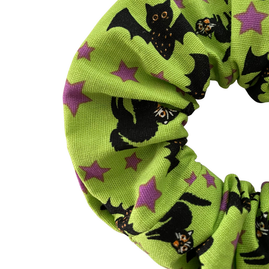 A close up view of a green scrunchie with black bats and black bats on a white background.