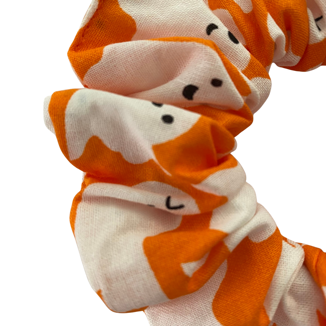 A close up view of our halloween scrunchie featuring white ghosts on orange soft cotton woven fabric.