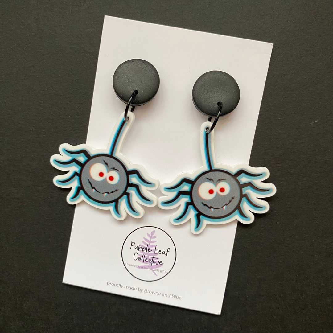 Spider-shaped earrings on a card with 'Purple Leaf Collective' branding against a dark background.