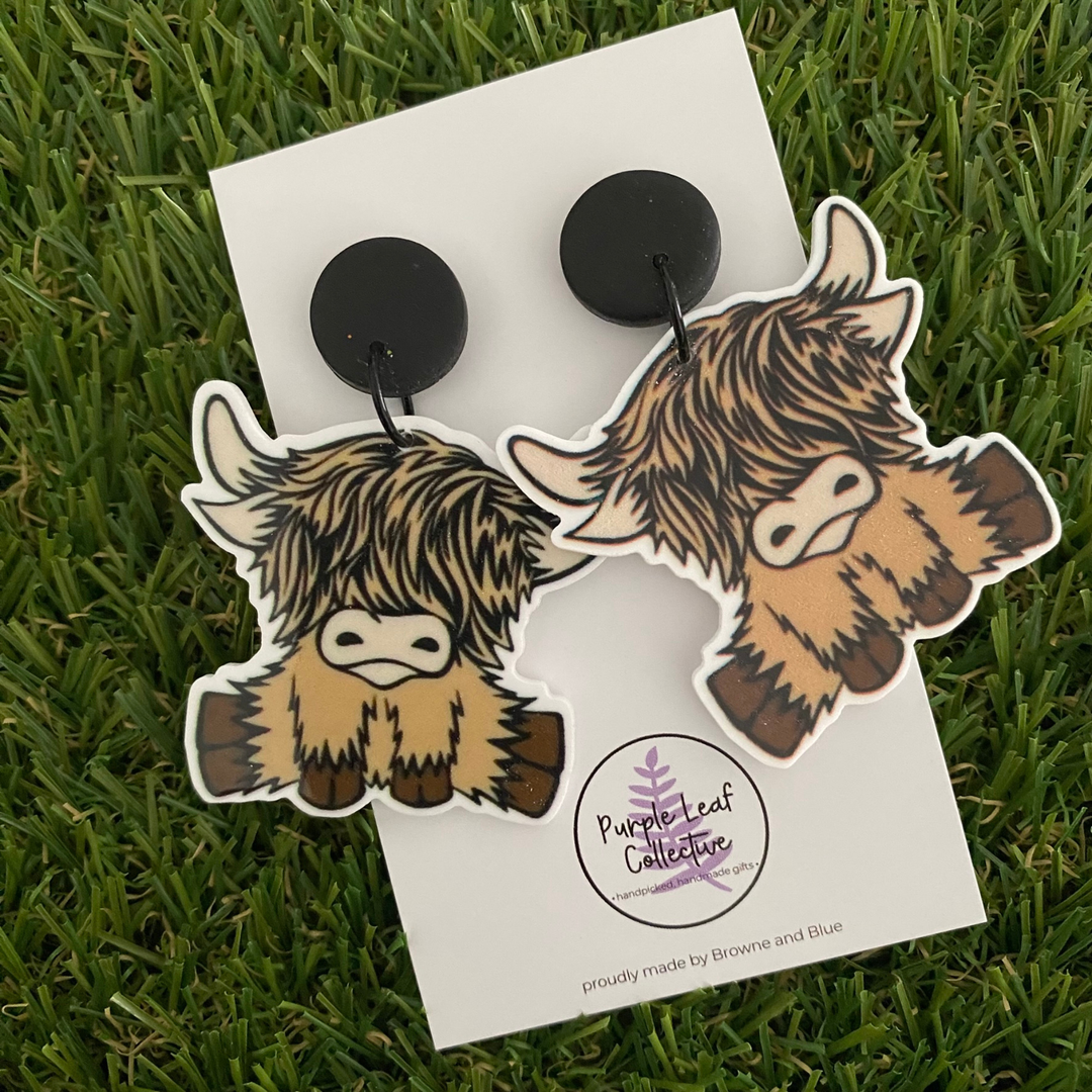 A pair of brown highland cow dangle earrings displayed on a backing card.