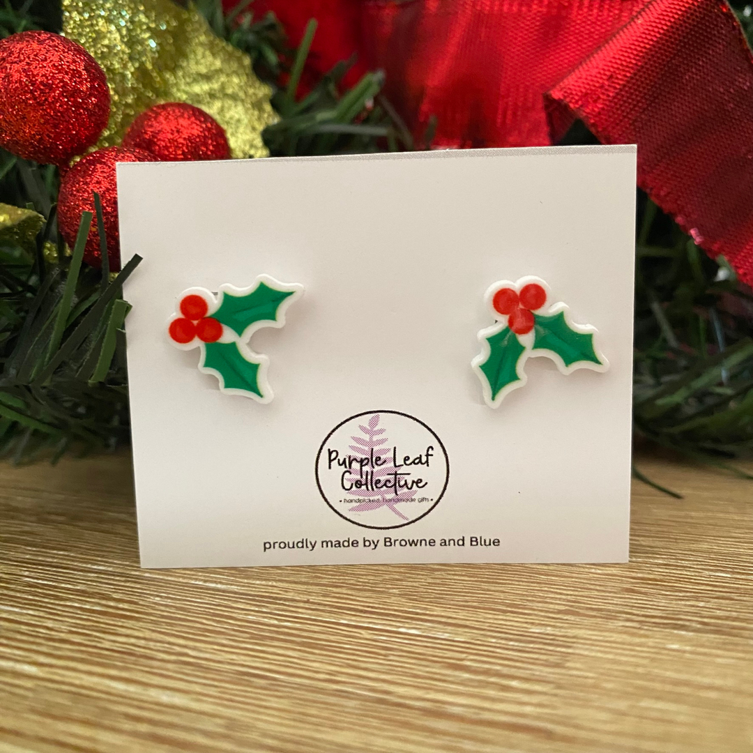 Holly leaf earrings on a card with Christmas decorations in the background.