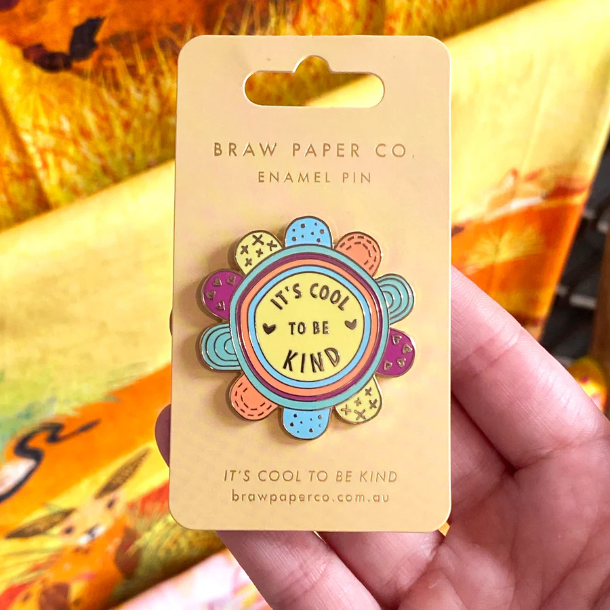 A picture of 'It's Cool To Be Kind' Enamel Pin, featuring a cheerful flower design with a charming illustrative detail