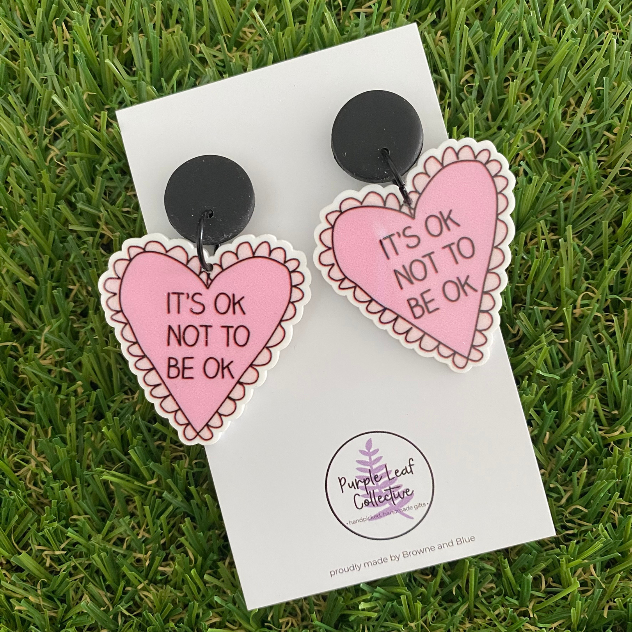 Heart-shaped dangle earrings with 'It's Ok Not To Be Ok' text on a white backing card.