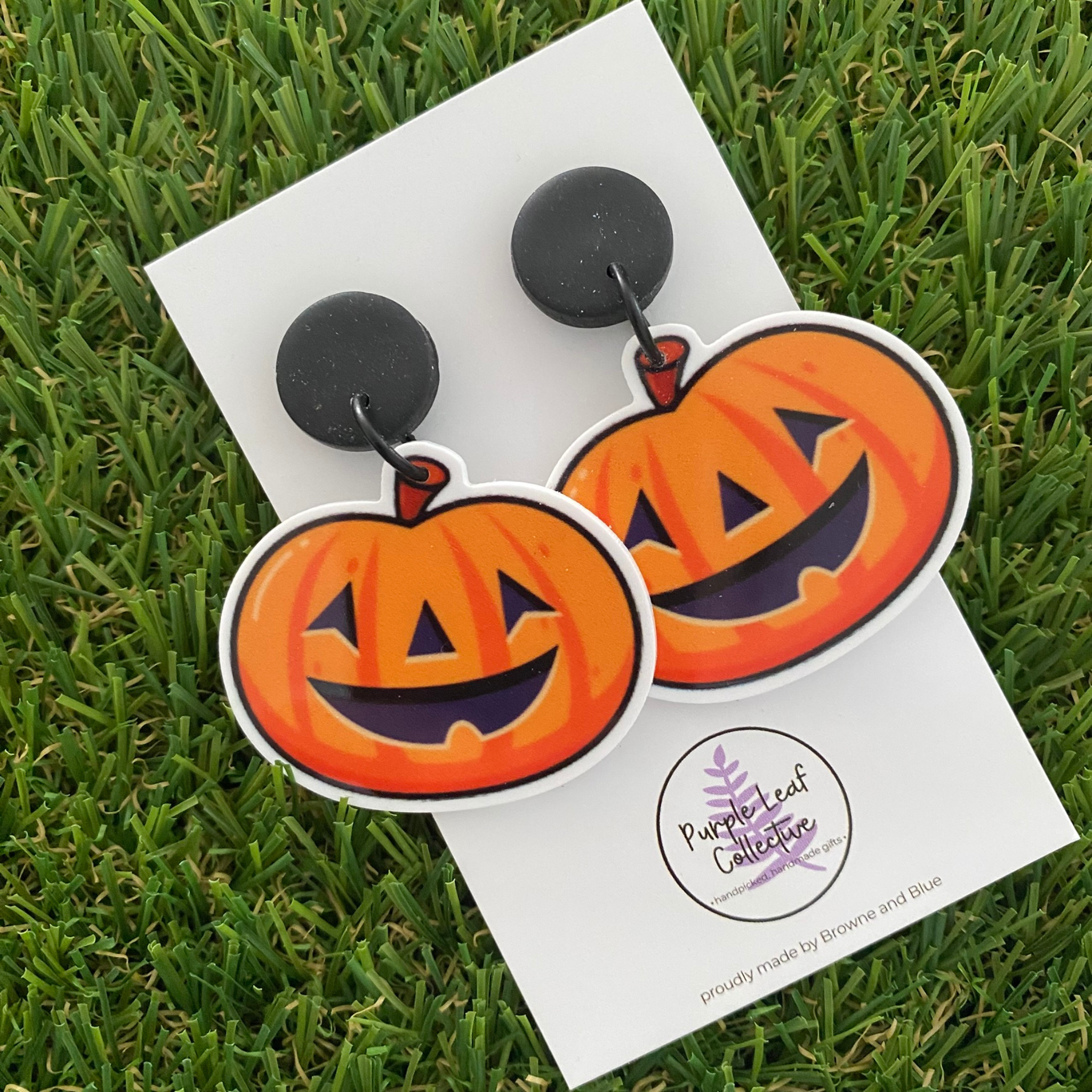 A pair of pumpkin shaped dangle earrings featuring cut-out faces on black clay tops.