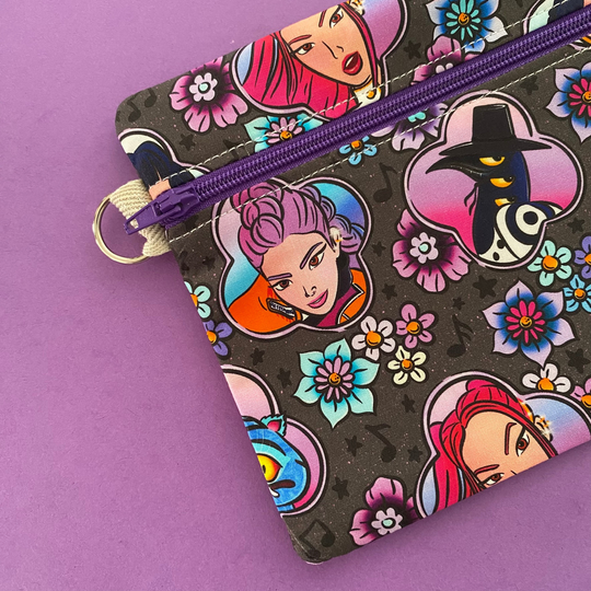 Side view of a small pouch with colourful character design and purple zipper on a purple background.