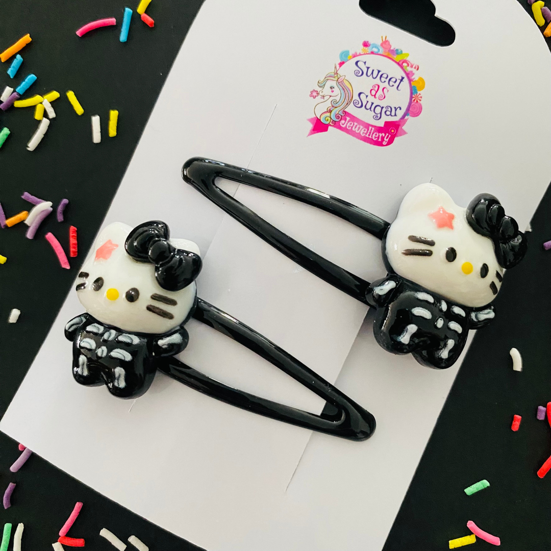A pair of black hair clips featuring a skeleton Hello Kitty charm.