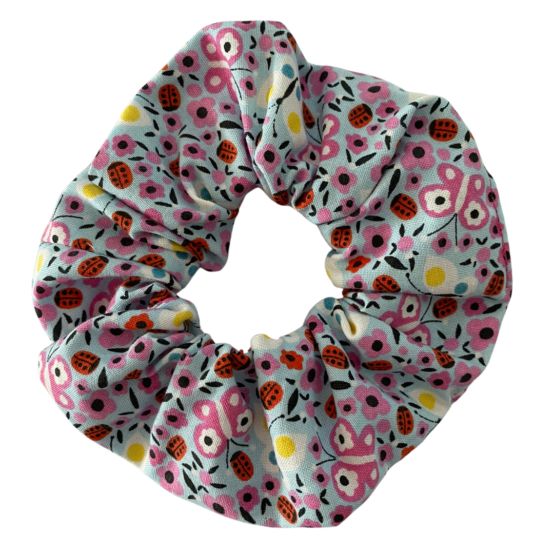 A light blue fabric scrunchie with images of ladybugs, butterflies and flowers.