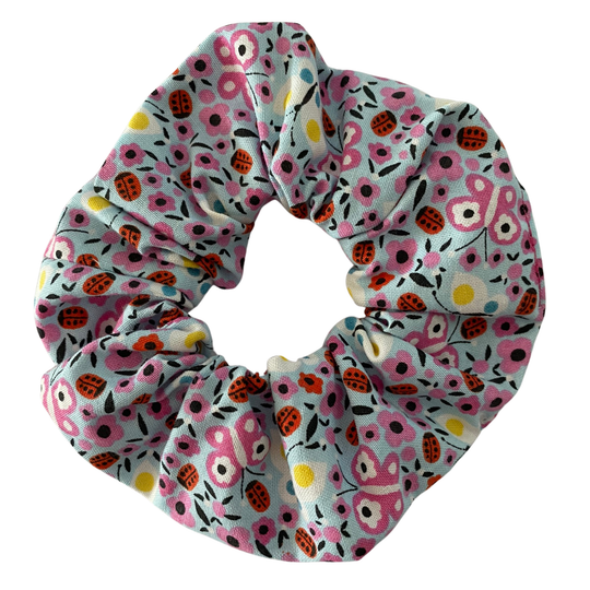 A light blue fabric scrunchie with images of ladybugs, butterflies and flowers.