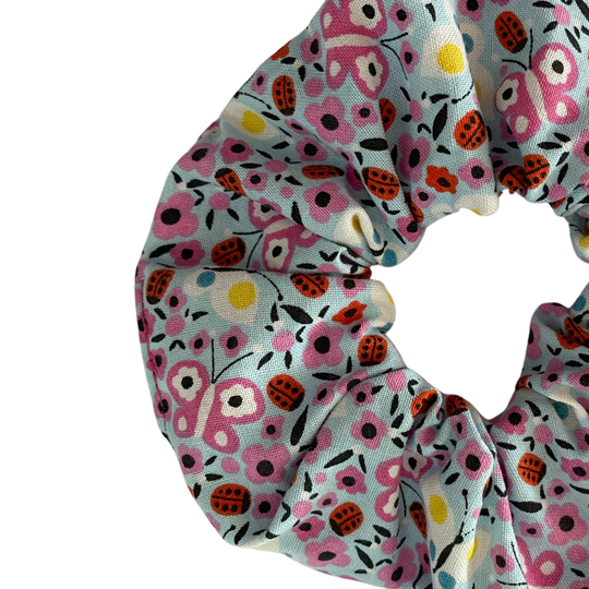 A close up view of a light blue fabric scrunchie with images of ladybugs, butterflies and flowers.