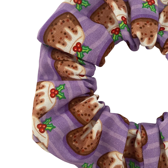 A close up view of a scrunchie with plum puddings on a purple background.