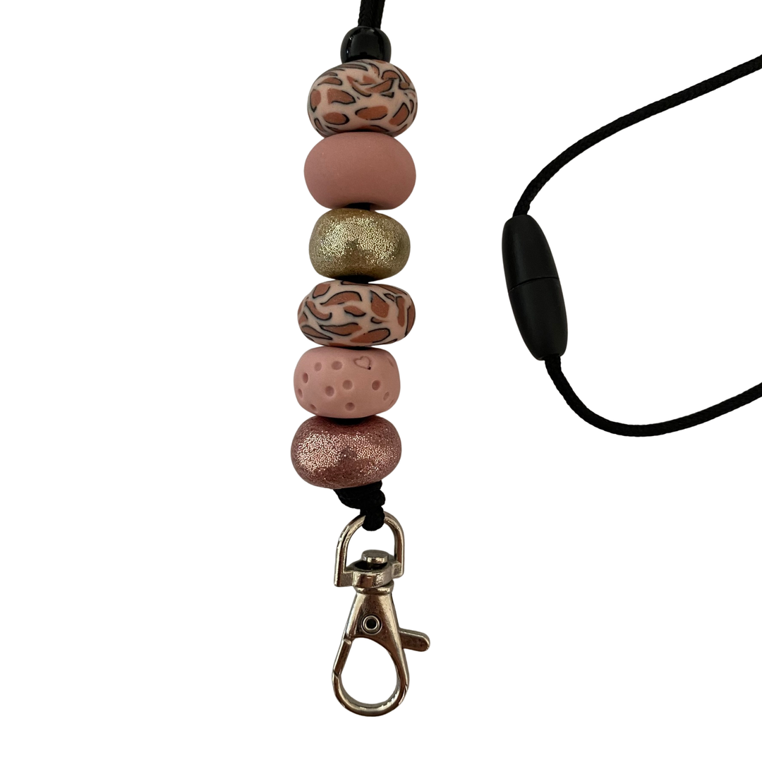 Handmade polymer clay lanyard with six hand-rolled beads in dusty pinks, leopard print, gold and pink glitter accents. Threaded on a nylon cord with a breakaway safety clasp and a silver-plated clip.