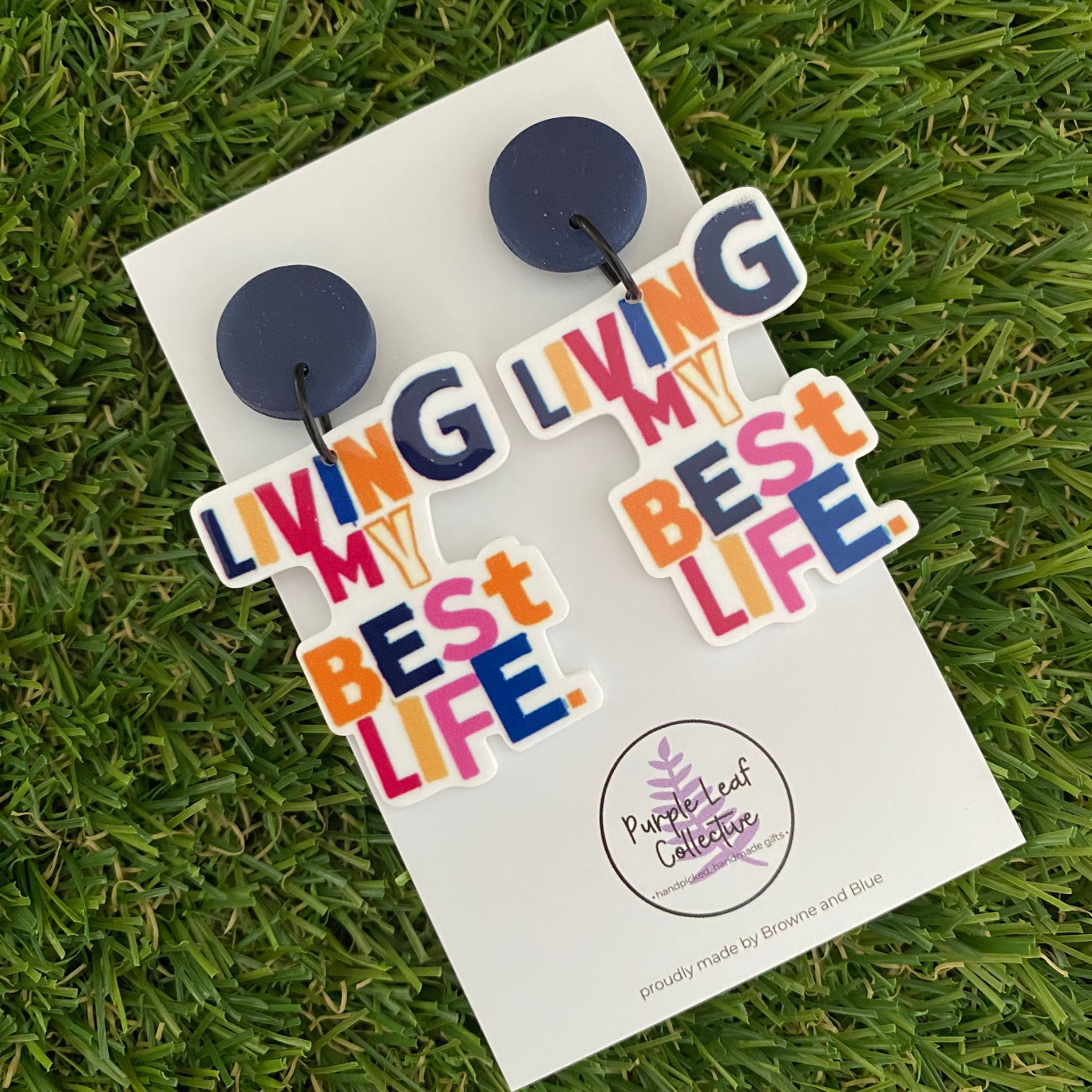 Earrings with 'Living My Best Life' text set on navy blue stud tops on a white backing card.