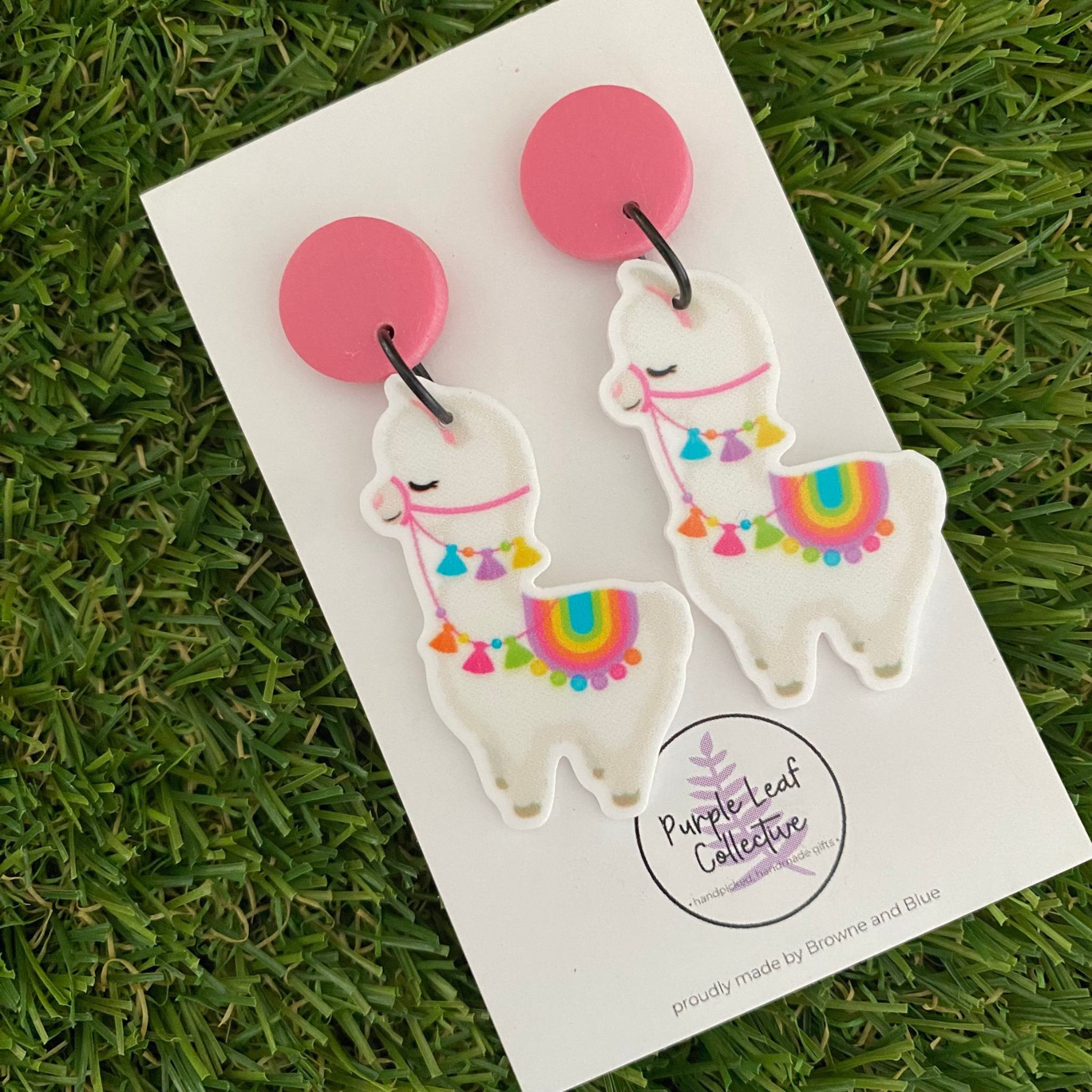 Dangle earrings featuring llamas with colourful tassel reins and a vibrant saddle set on dusty pink clay tops.