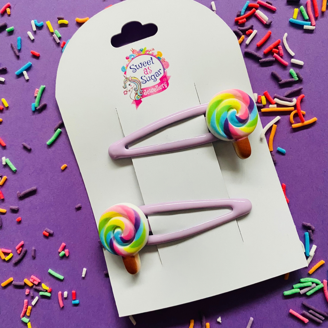 Two lavender hair clips with colourful rainbow swirl lollipop charms.