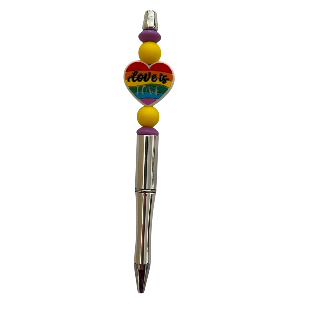 Pen with colorful heart-shaped bead and rainbow-colored beads and the words love is love on a white background.