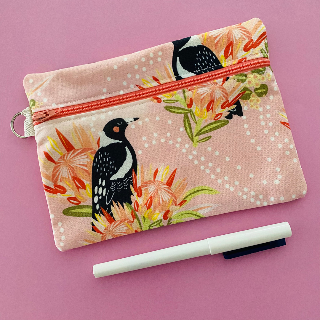 Fabric pouch with a Magpie and floral design on a light pink background.