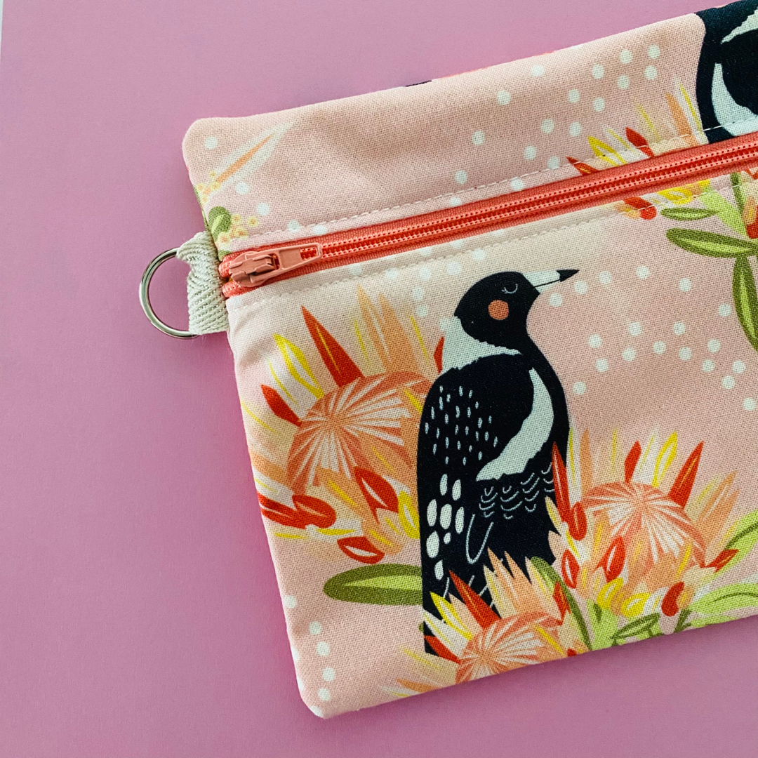 Fabric pouch with a Magpie and floral design on a light pink background with  a sewen in D-ring.