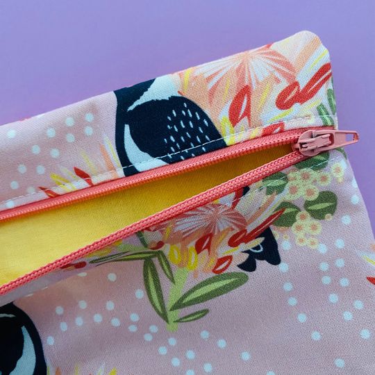 Fabric pouch with a Magpie and floral design with yellow lining and apricot zipper.