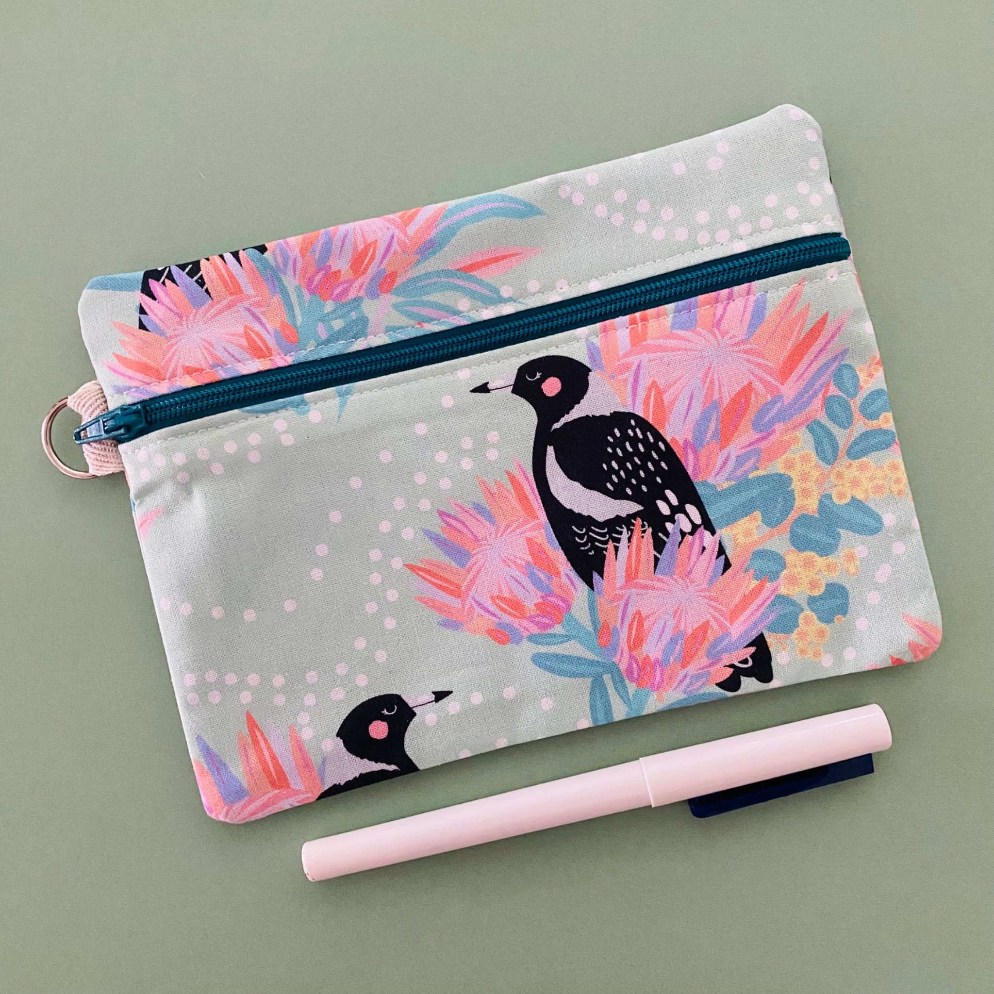 Fabric pouch with a Magpie and floral design on a light green background.