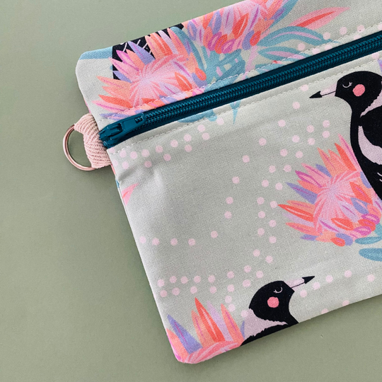Fabric pouch with a Magpie and floral design on a light green background with  a sewen in D-ring.