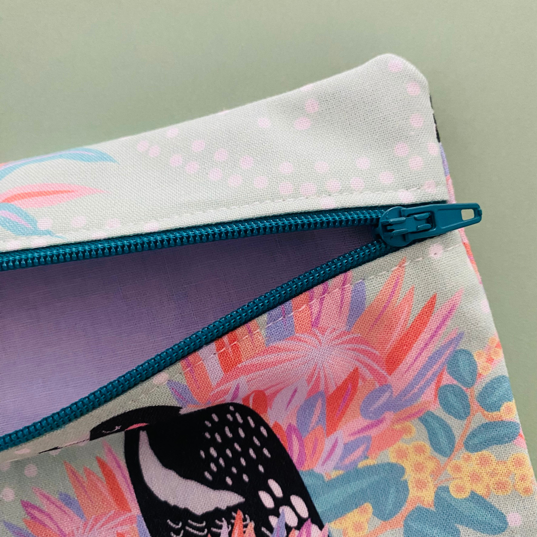 Fabric pouch with a Magpie and floral design with lilac lining and teal zipper.