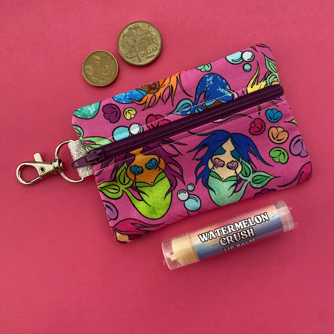 A clip coin purse with images of mermaids on a hot pink fabric.