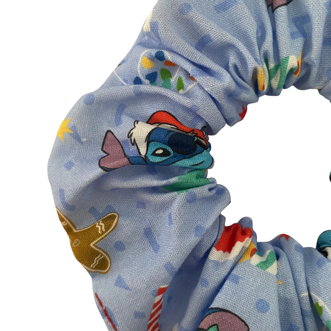 Close up view of a light blue scrunchie featuring images of Stitch and other festive images.