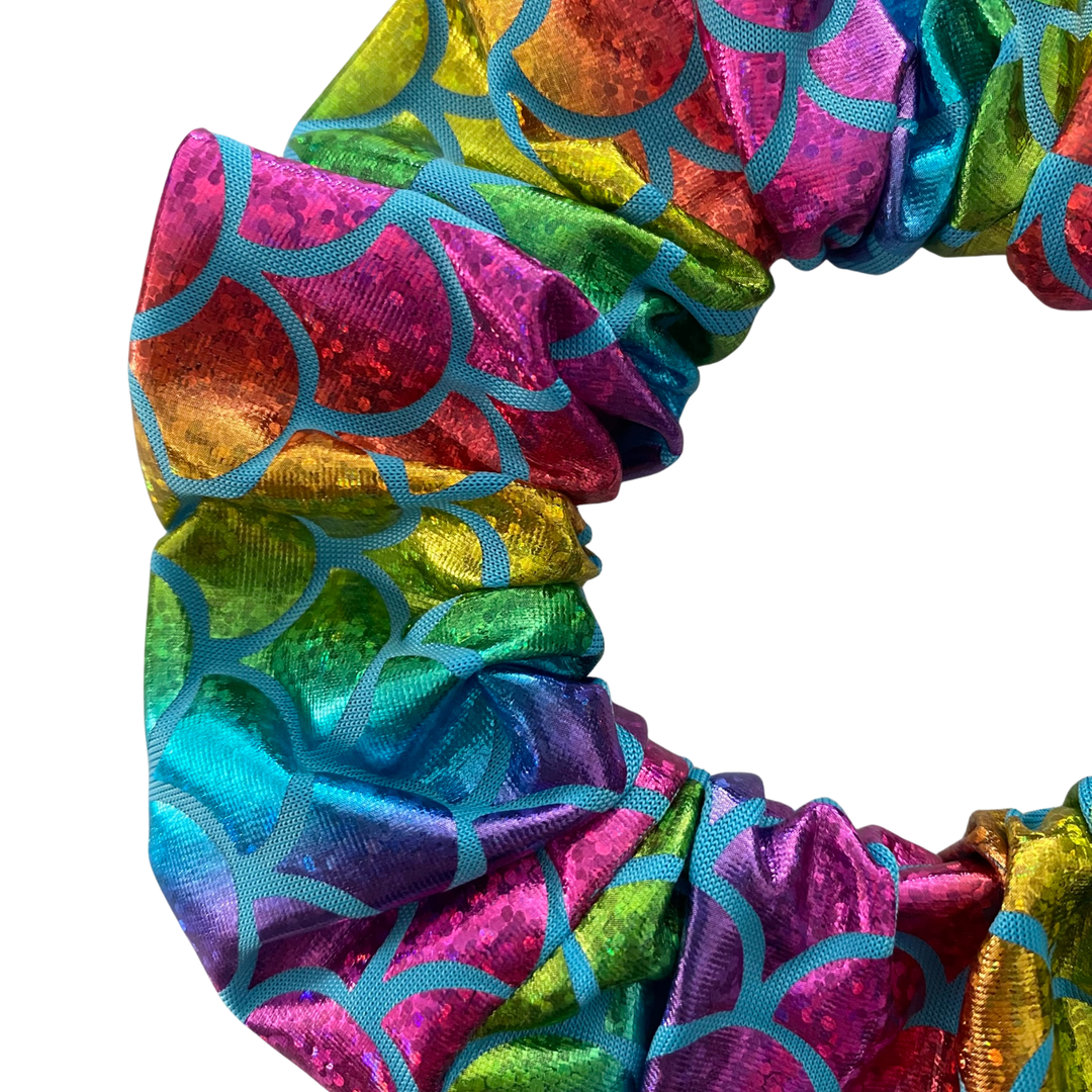 Detailed close-up of the shimmering metallic fabric and rainbow scale pattern on a stretchy, handmade hair scrunchie.
