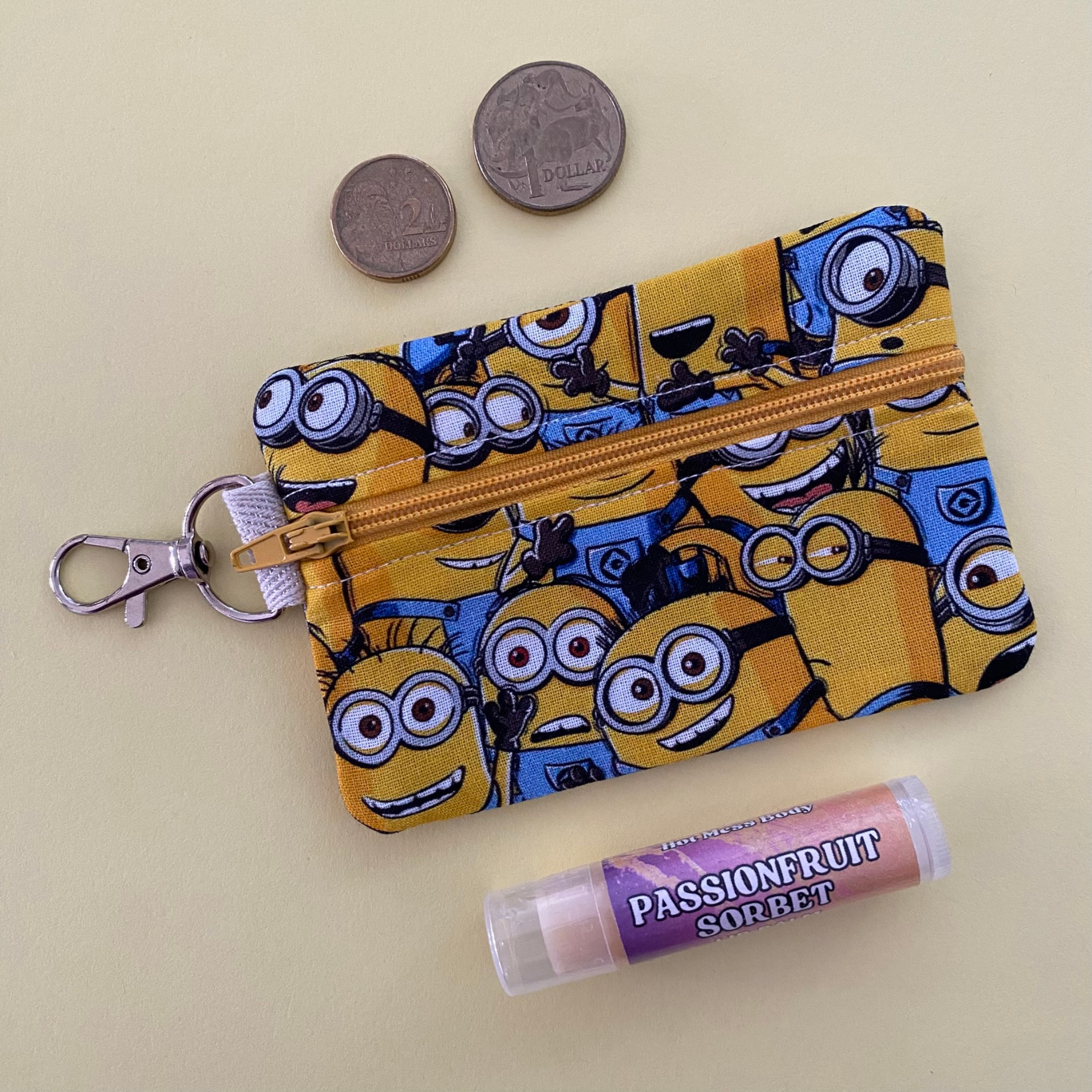 Minion-themed pouch with a keychain, coins, and a lip balm on a beige background