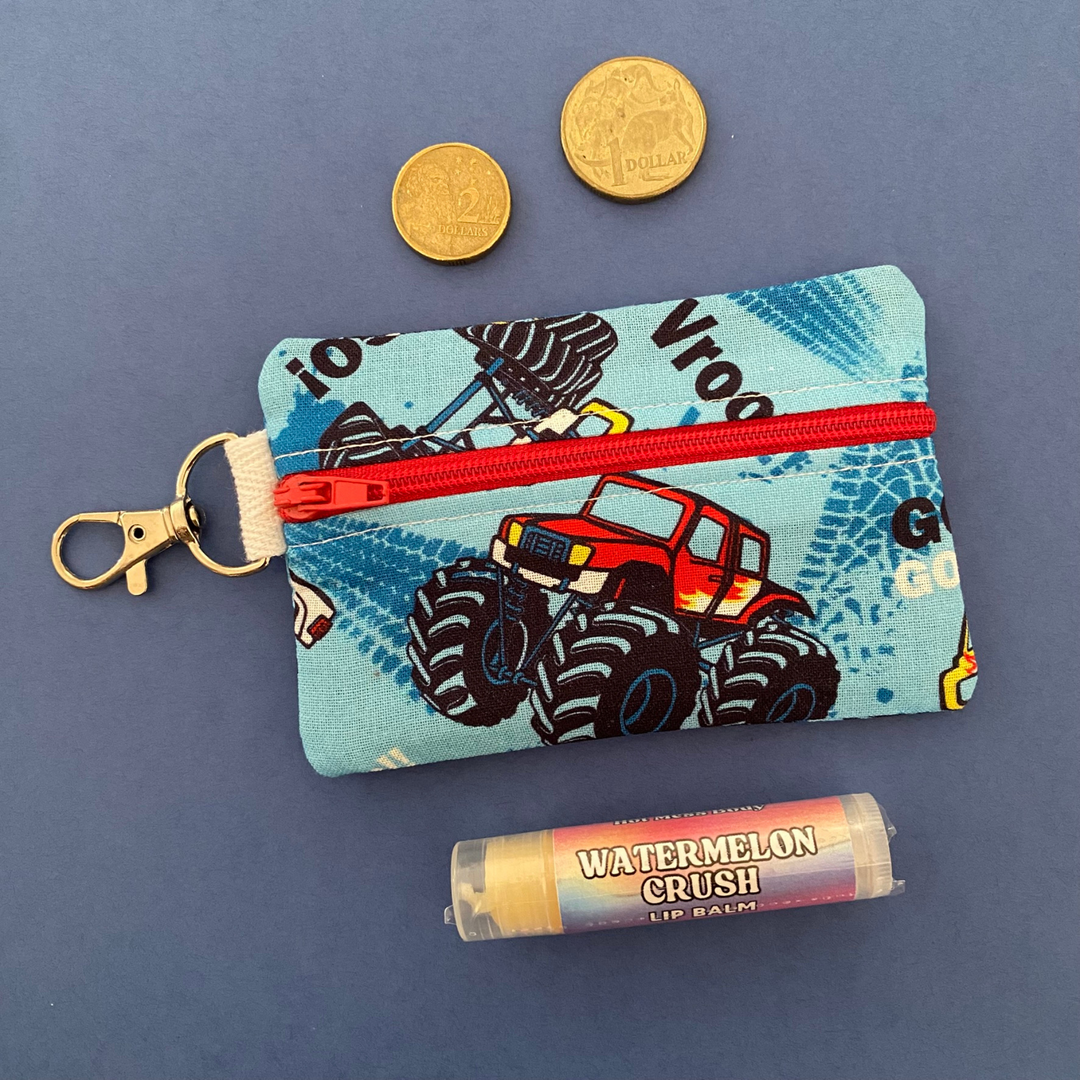 A small clip coin purse perfect for coins and small essentials with bold and exciting monster truck imagery on a light blue fabric.
