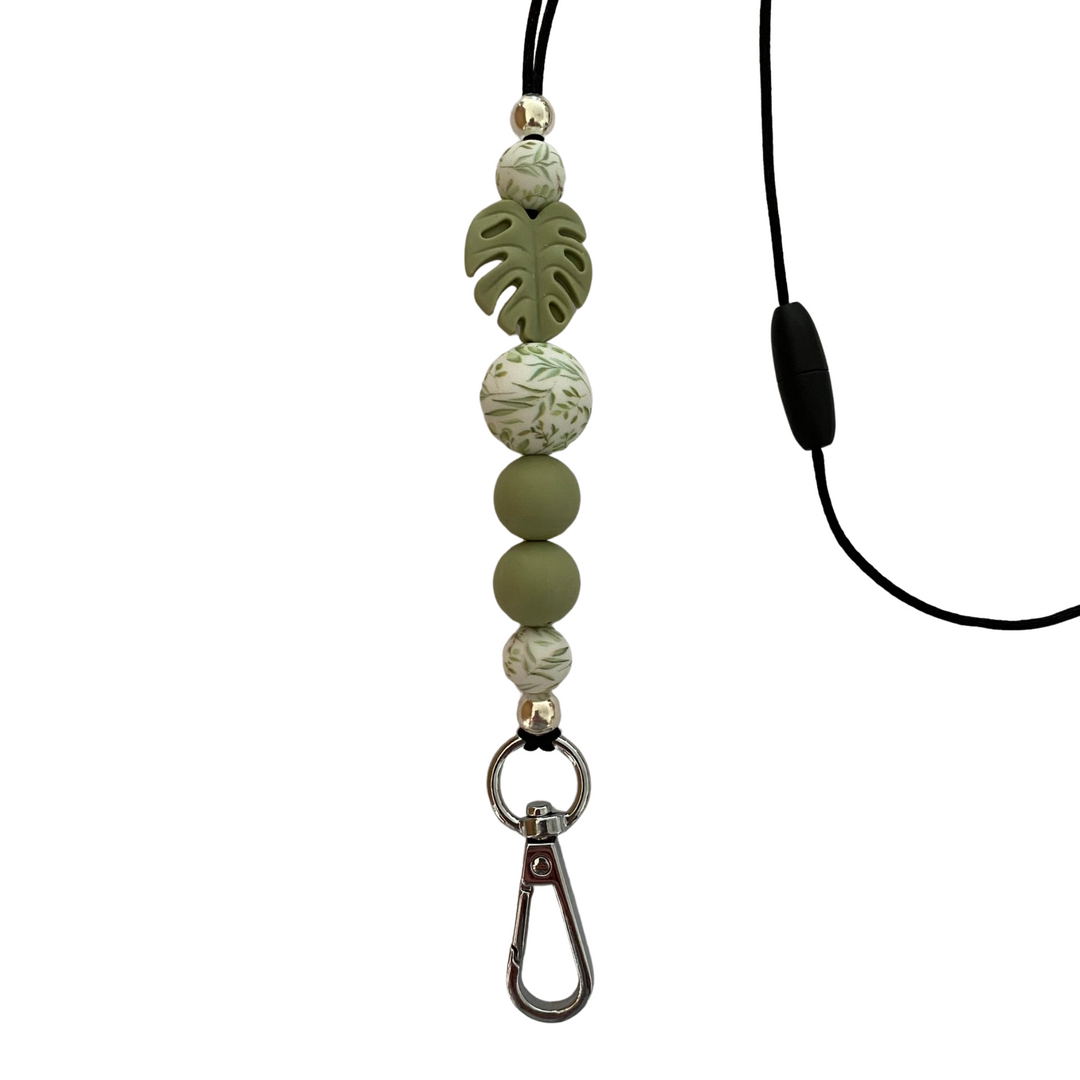 A 60cm black cord lanyard with breakaway clasp with a Green Monstera Leaf silicone bead and other coloured silicone beads.