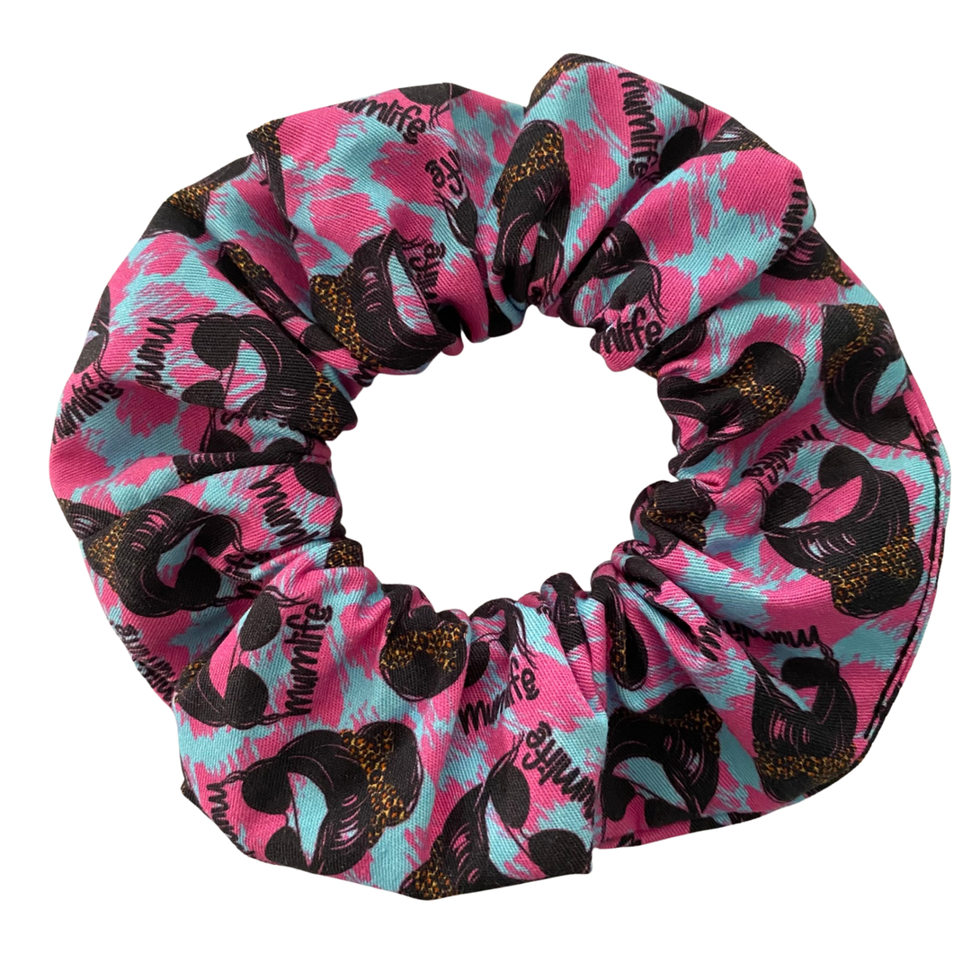 A hot pink and blue fabric scrunchie with images of a woman rocking sunglasses and a messy bun, complete with her own bow scrunchie.