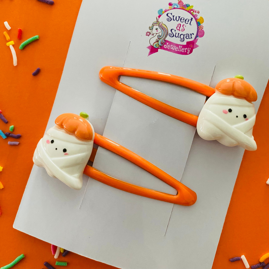 Halloween-themed hair clips with mummified ghost and pumpkin hats on orange clips.