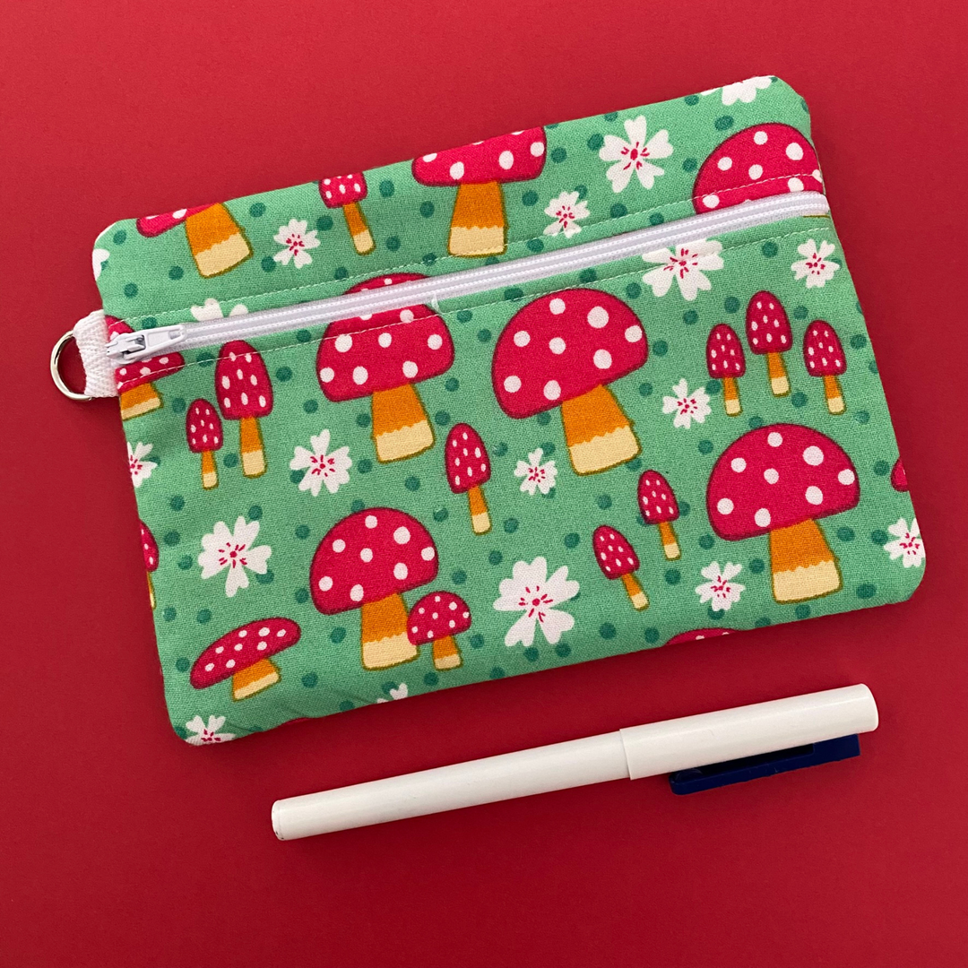 Zipper pouch with images of Red Mushrooms on a green fabric. Planner accessory for school or work. Perfect for small essentials.