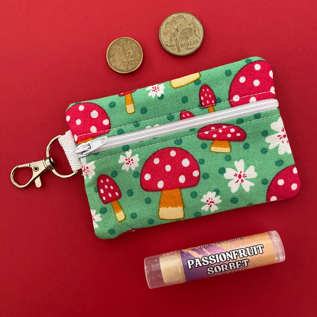 A small clip coin purse perfect for coins and small essentials decorated with vibrant red mushroom illustrations.