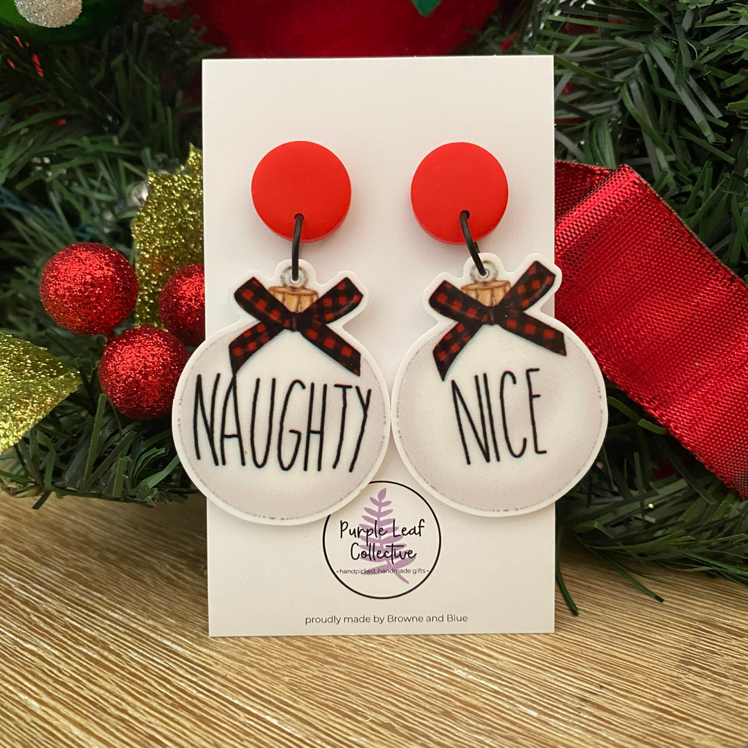 Christmas-themed naughty nice baubles earrings on a card with 'Purple Leaf Collection' branding, surrounded by festive decorations.