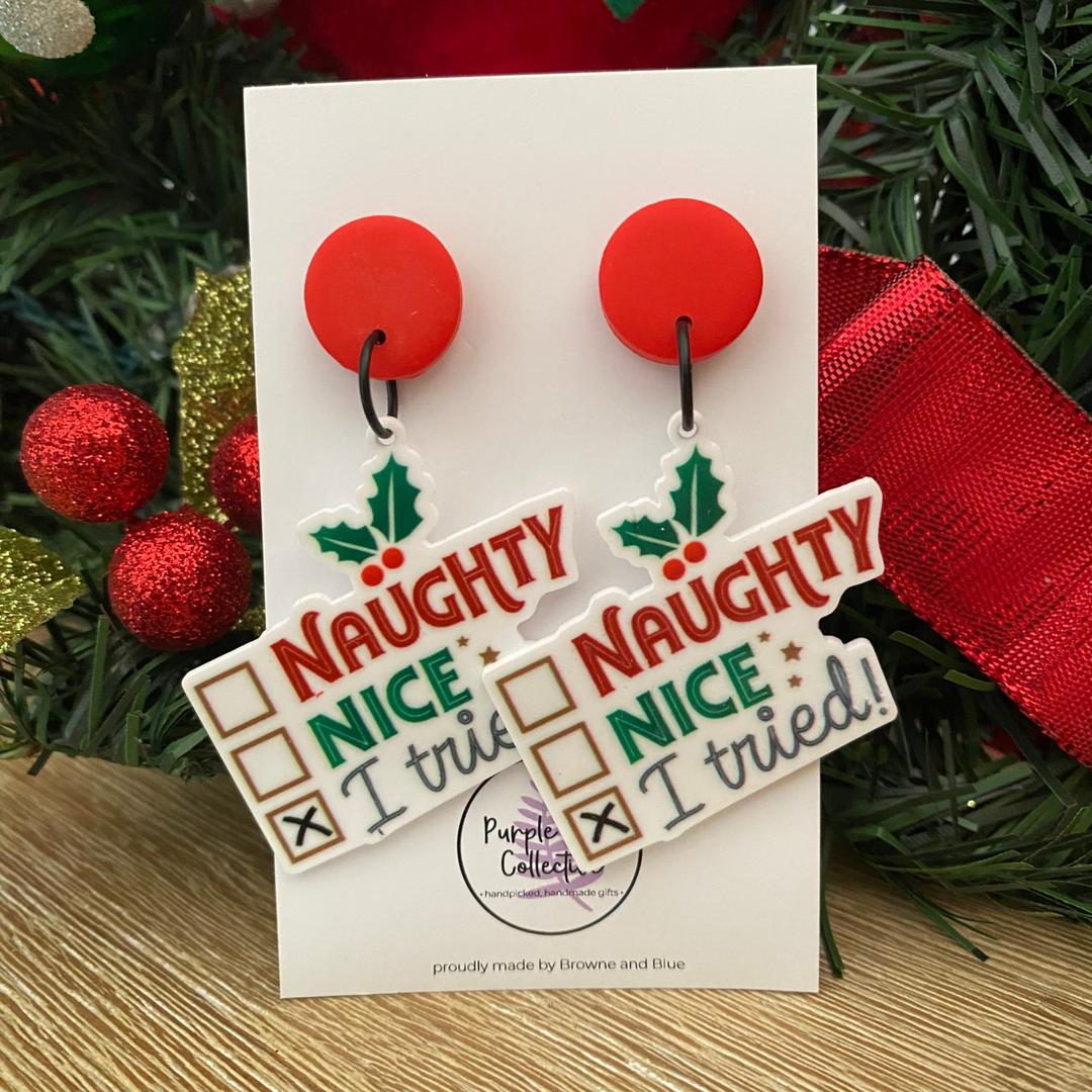 Pair of earrings with 'Naughty Nice I tried' design on a card with Christmas decorations.