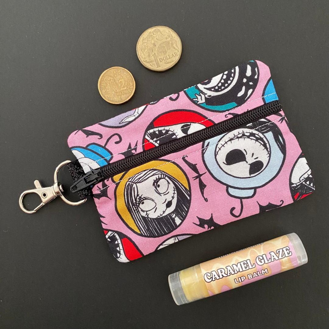 A small clip coin purse perfect for coins and small essentials featuring the characters from The Nightmare Before Christmas on dusty pink fabric.