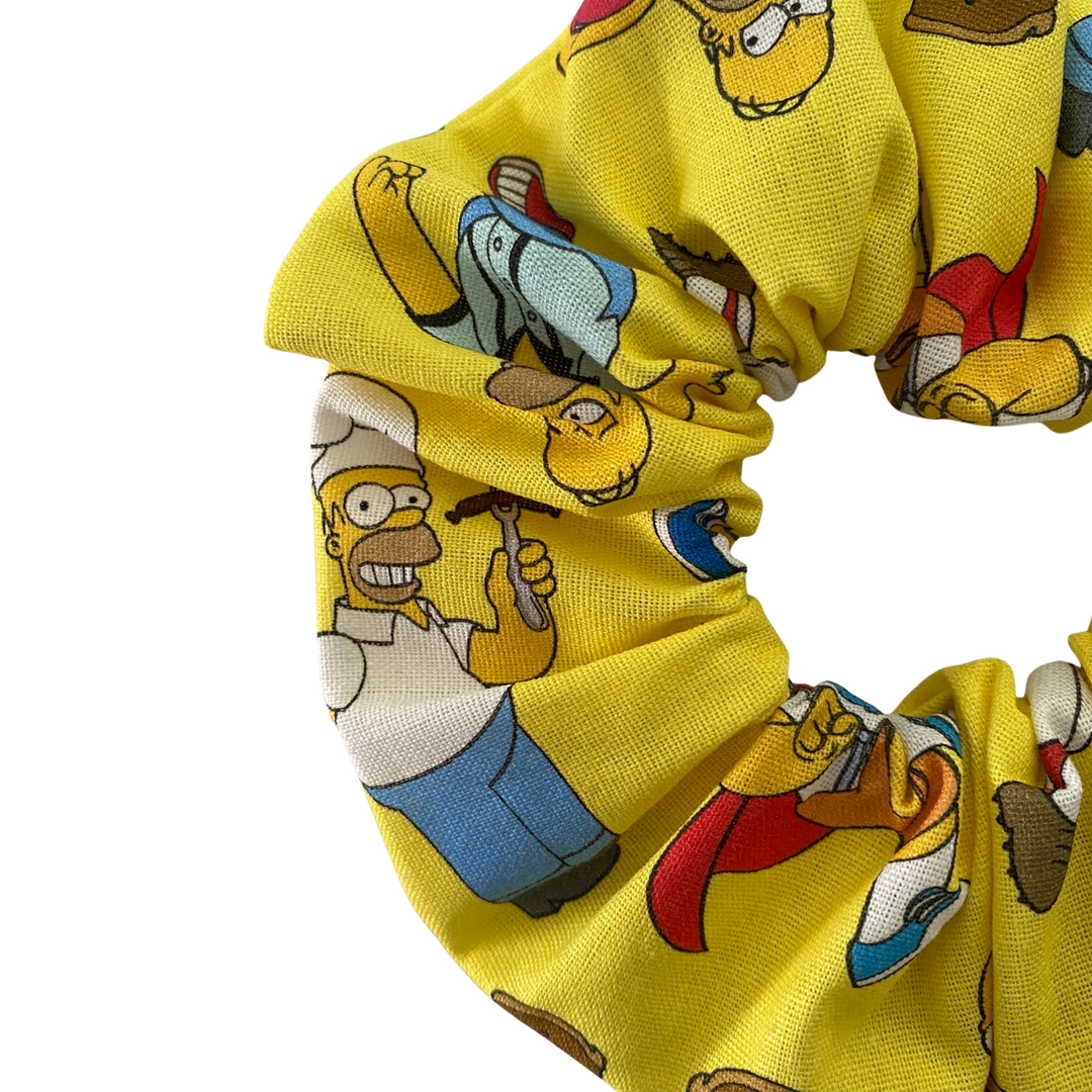 Close up view of yellow scrunchie with Homer Simpson character pattern on a white background.
