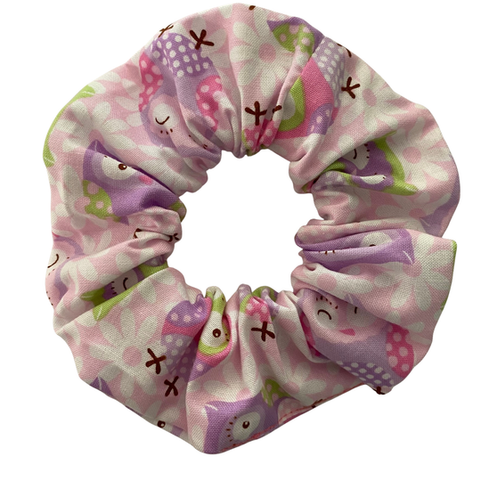 A light pink scrunchie with images of owls in pink, lilac, and purple hues.