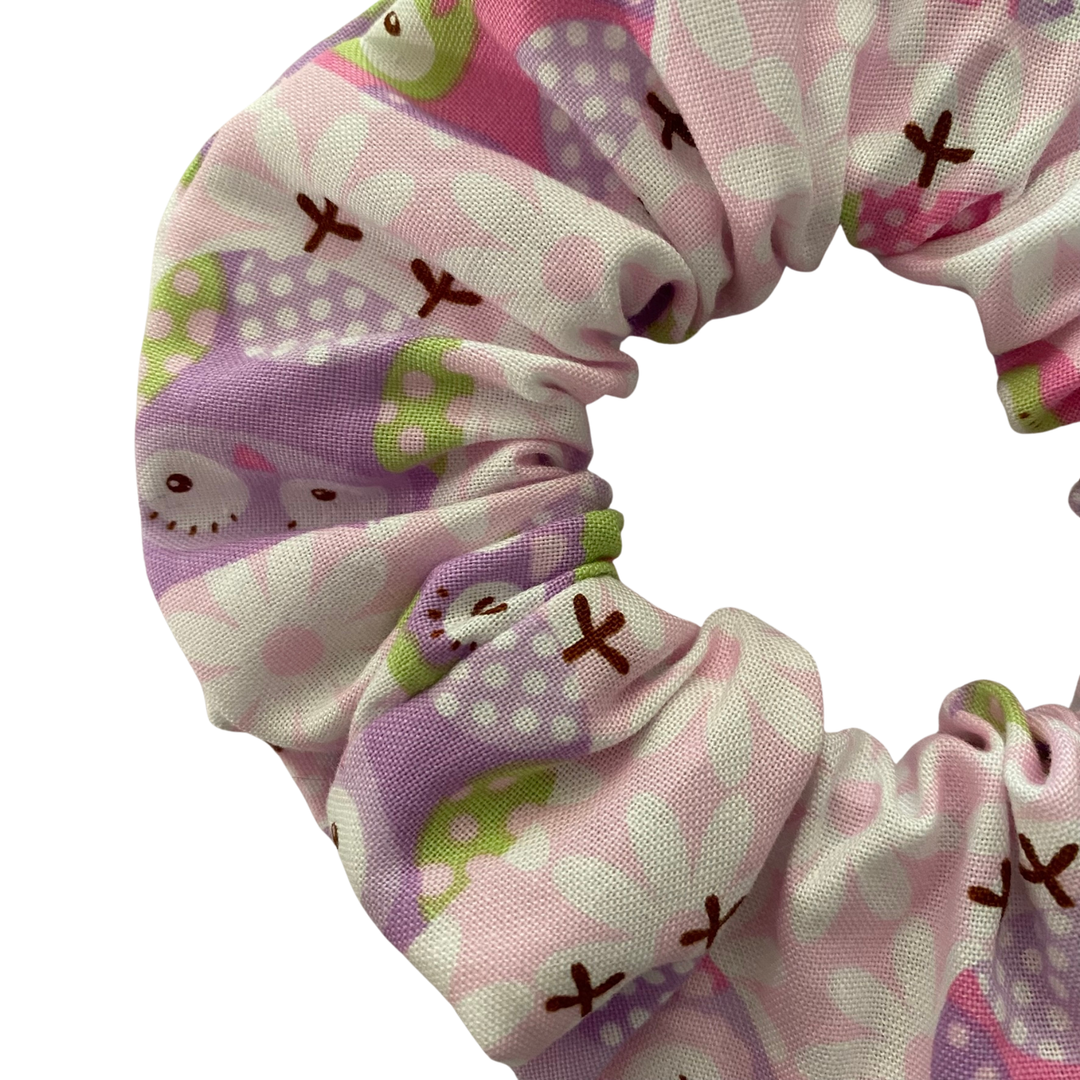 Close up view of a light pink scrunchie with images of owls in pink, lilac, and purple hues.