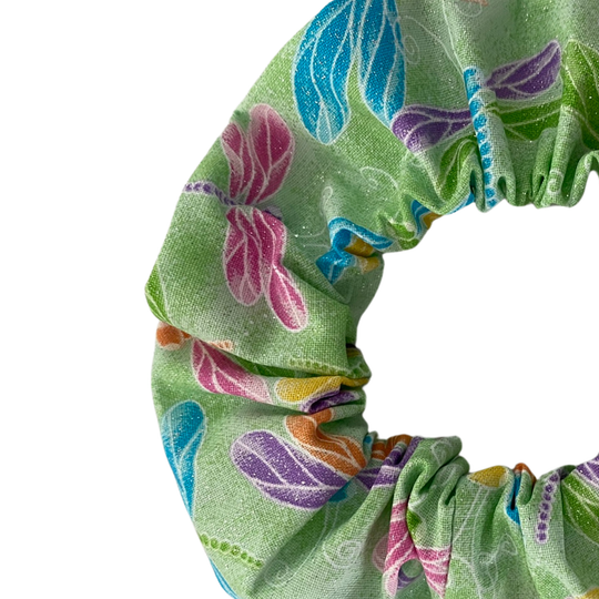A close up view of a lime green scrunchie with images of pink, purple, blue, orange and yellow dragonflies with added glitter.