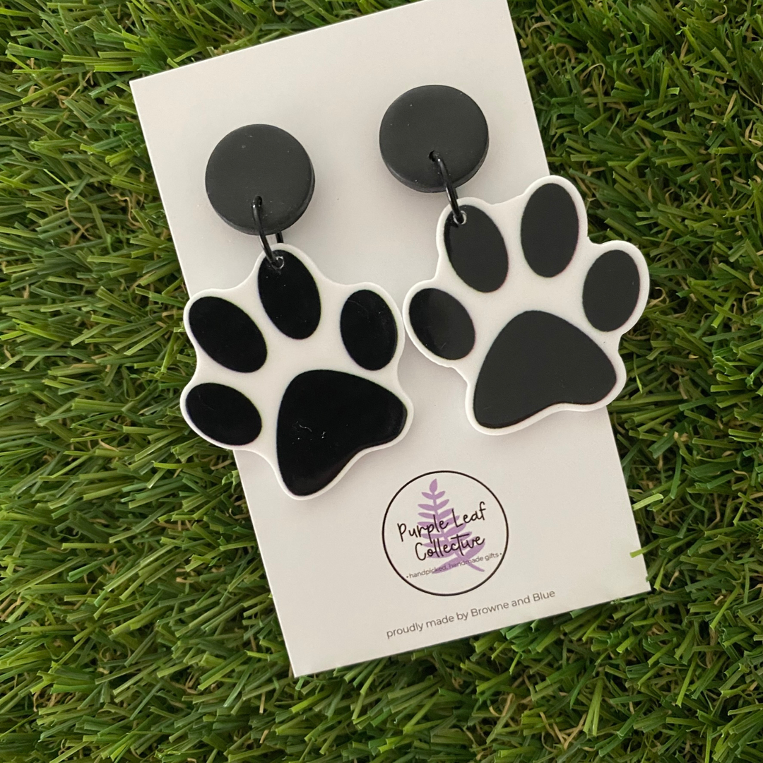 A pair of black paw print dangle earrings on a backing card.