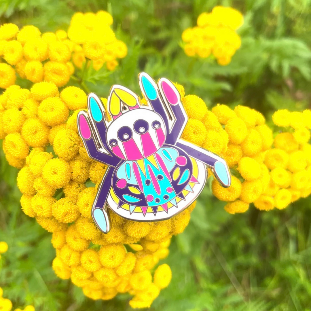 Colorful spider-shaped pin on yellow flowers with a green blurred background.